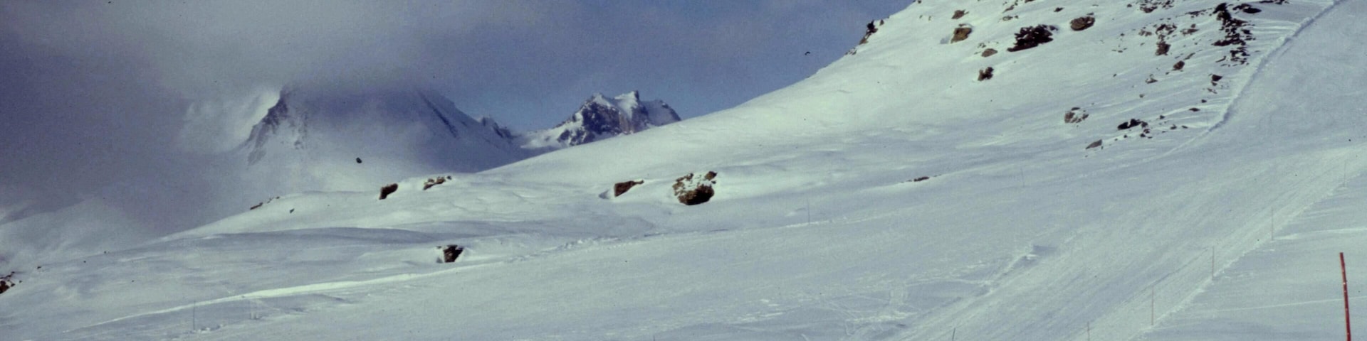 A snow-covered mountain slope with a clear sky and a few scattered rocks.