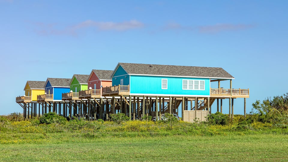 A row of colorful wooden houses on stilts in a grassy field.