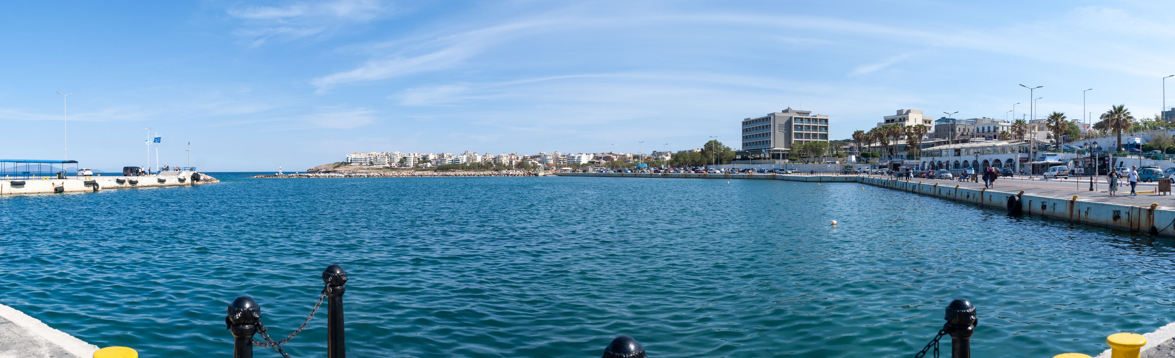 A coastal cityscape with a marina, buildings, and a clear blue sky.