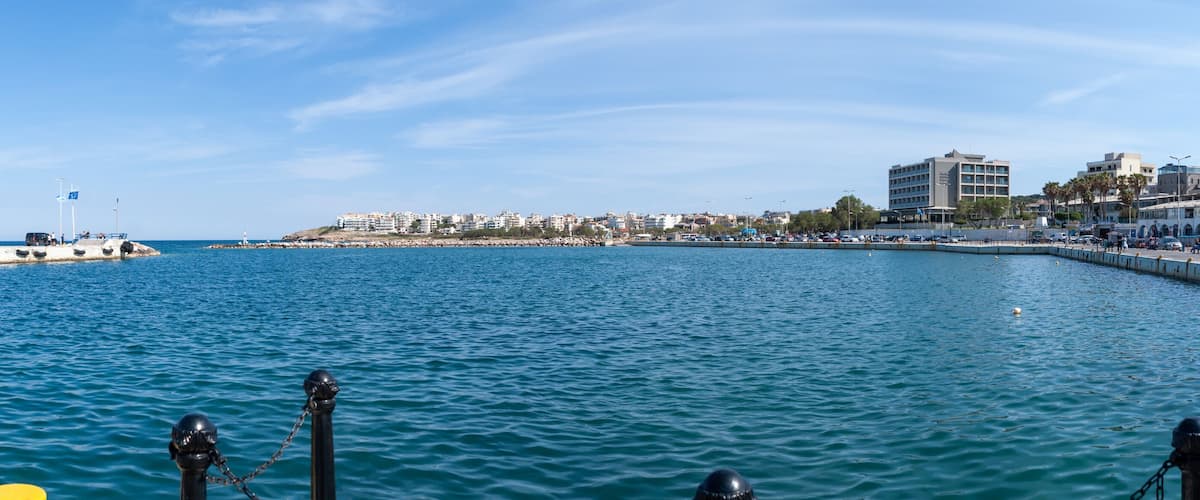 A coastal cityscape with a marina, buildings, and a clear blue sky.
