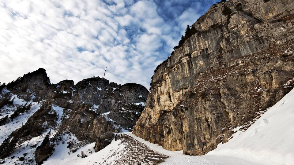 A snow-covered mountain with rocky cliffs and a clear sky.