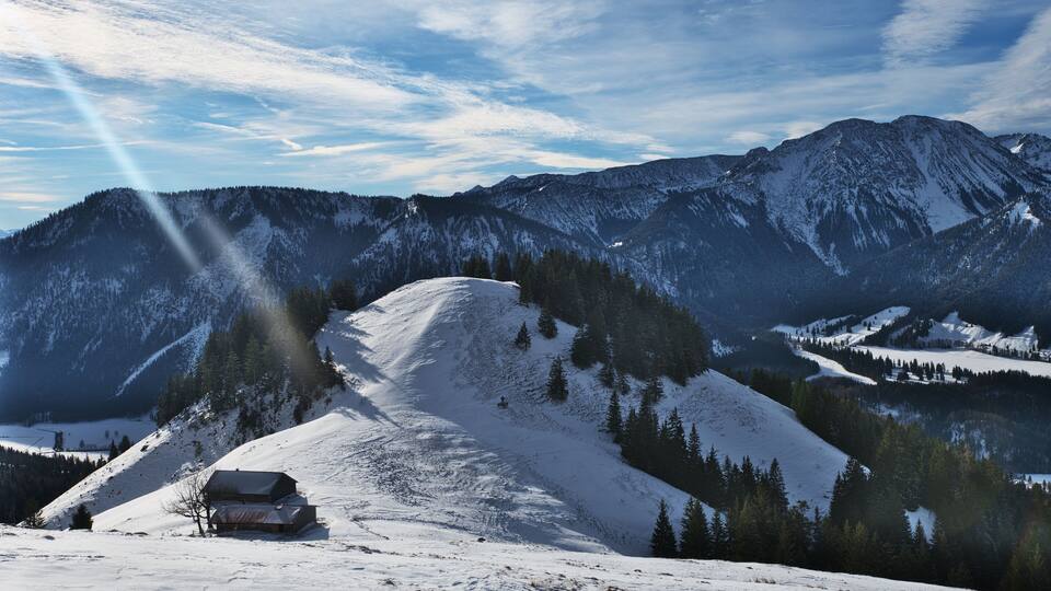 A snow-covered mountain landscape with a cabin and dense forest.