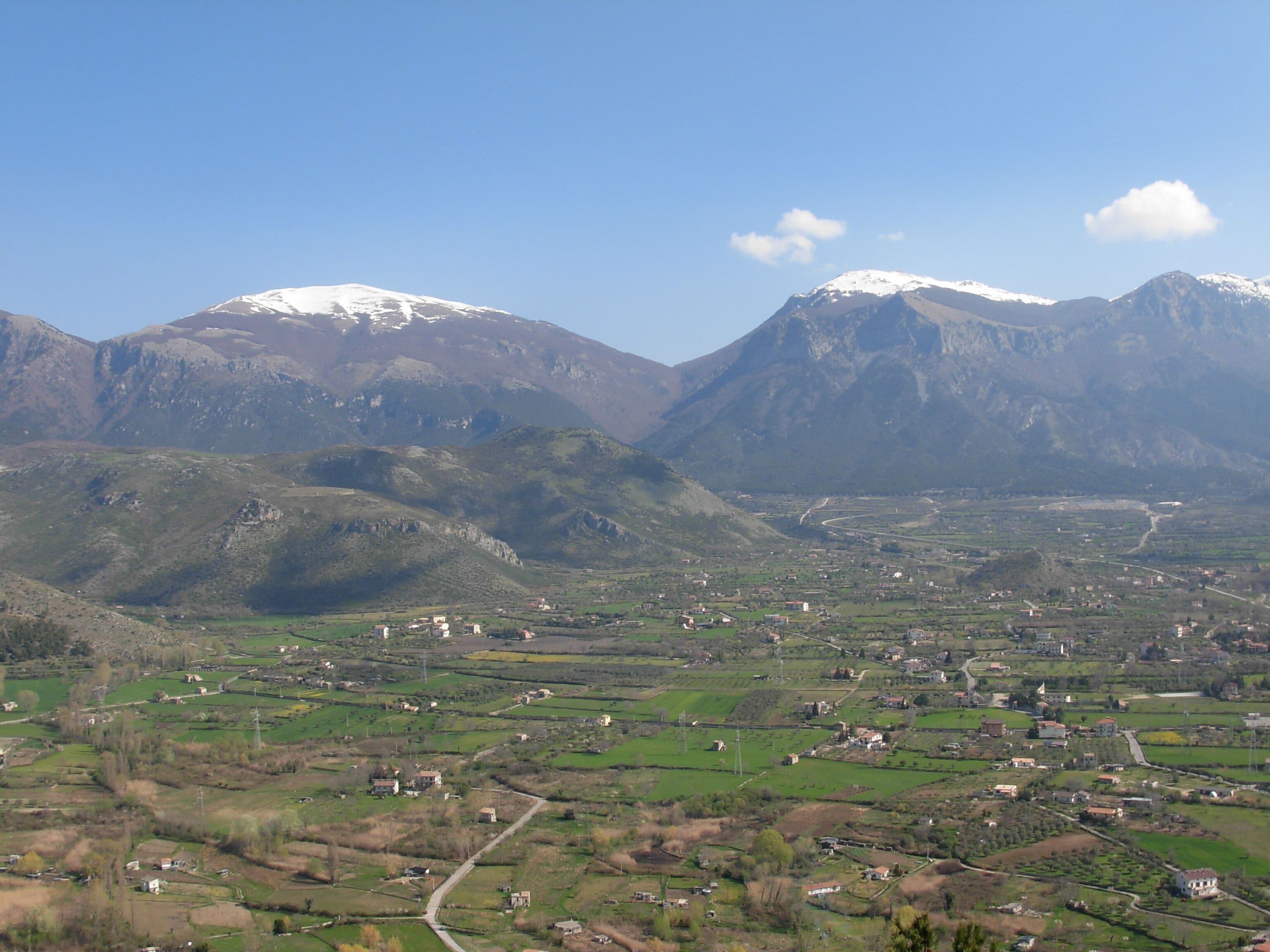 A valley with scattered houses and snow-capped mountains in the background.