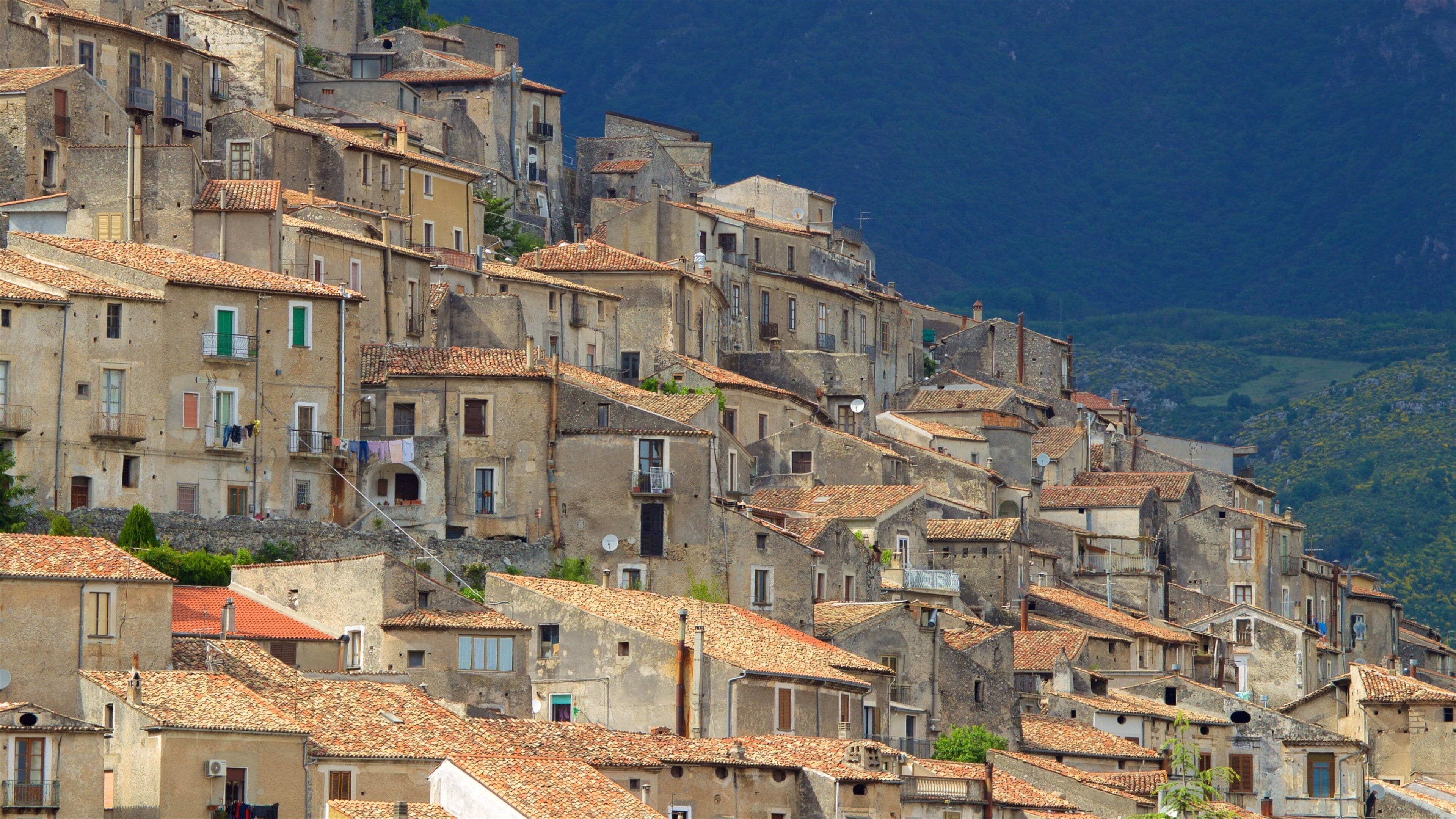 A hillside of terracotta-roofed buildings with balconies and a mountainous backdrop.