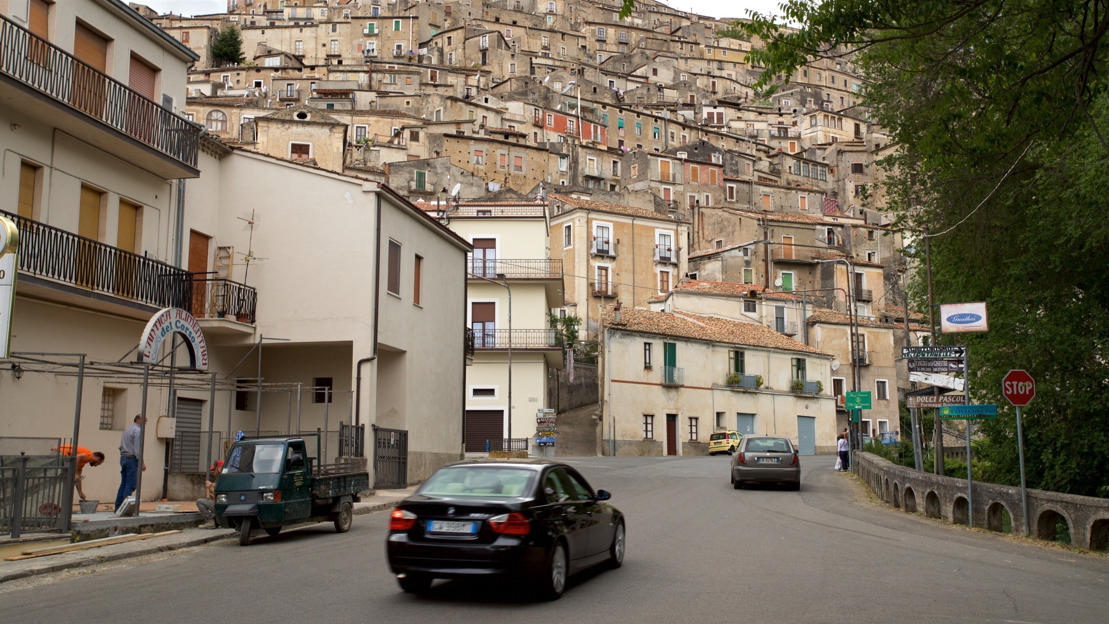 A narrow street in a densely packed urban area with historic buildings and a steep hill in the background.