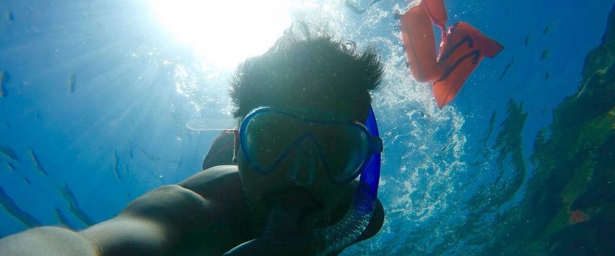 A person snorkeling underwater with a bright light source above.
