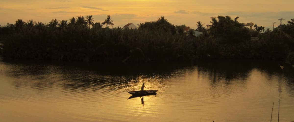 A sunset over a calm body of water with a silhouette of a person in a boat.