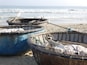 Three boats on a sandy beach with the ocean in the background.