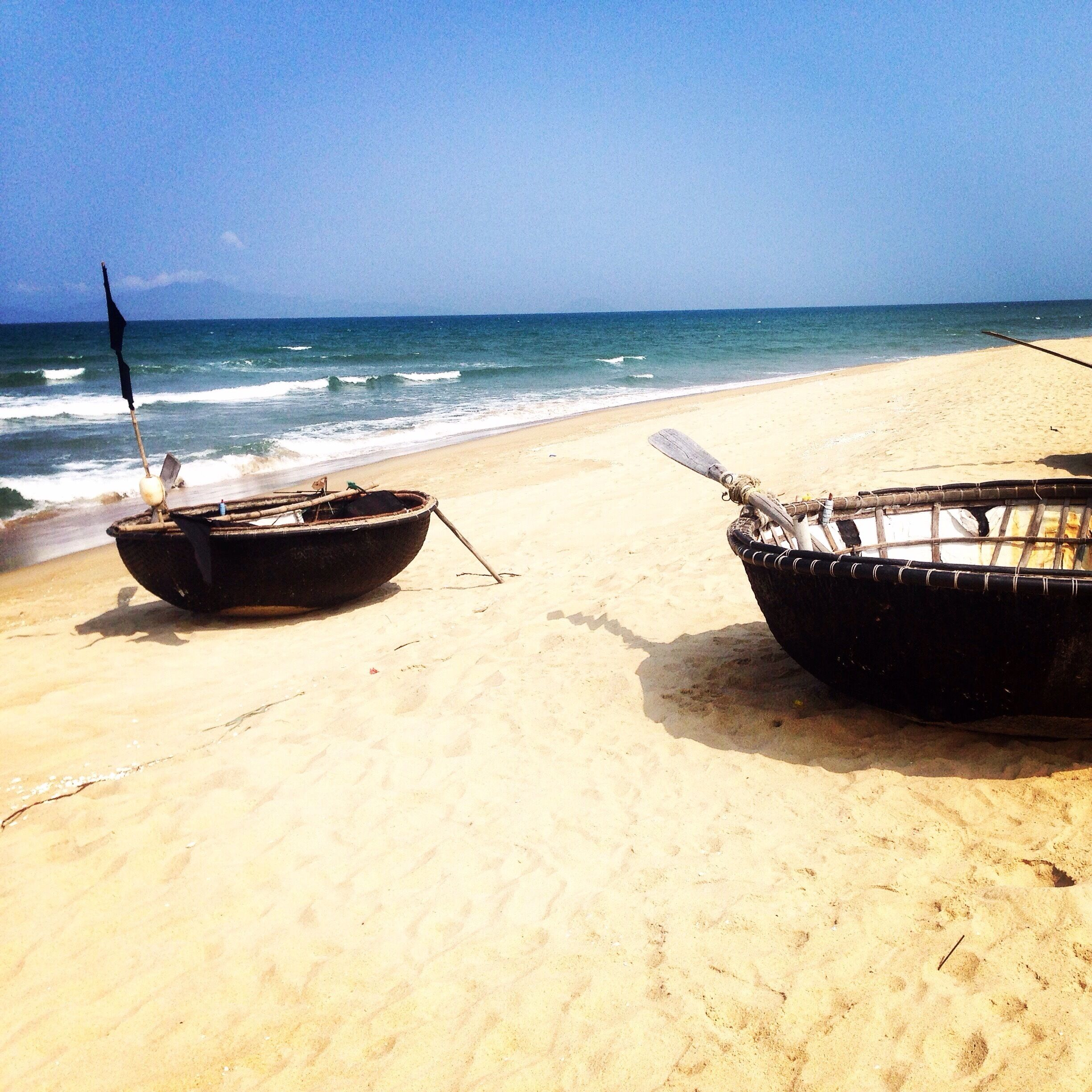 Dos barcos en una playa arenosa con el océano al fondo.