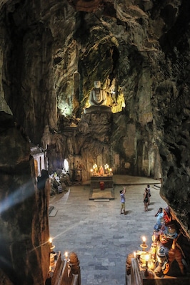A cave temple with a large Buddha statue, altars, and visitors.