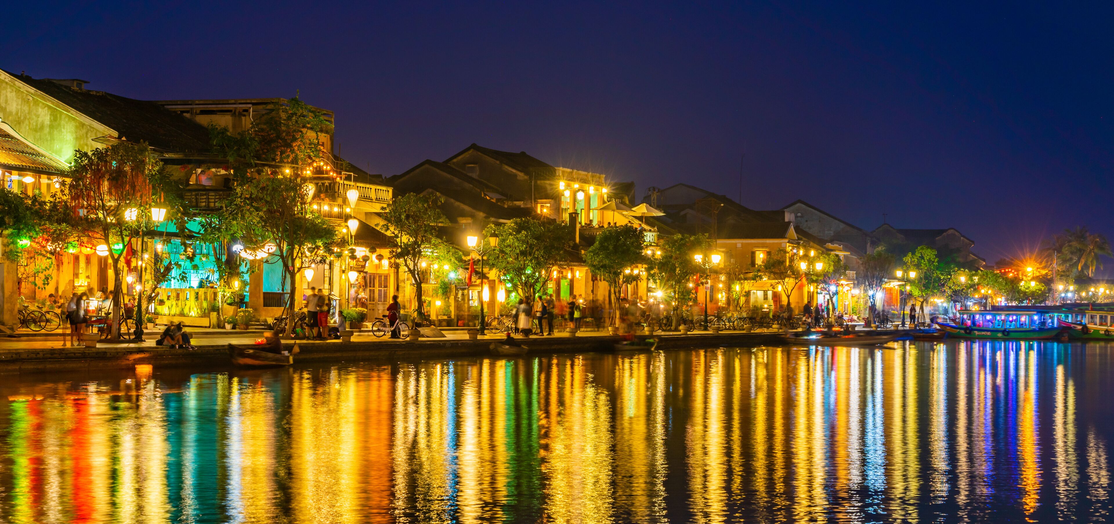 A riverside with illuminated buildings reflecting on the water.