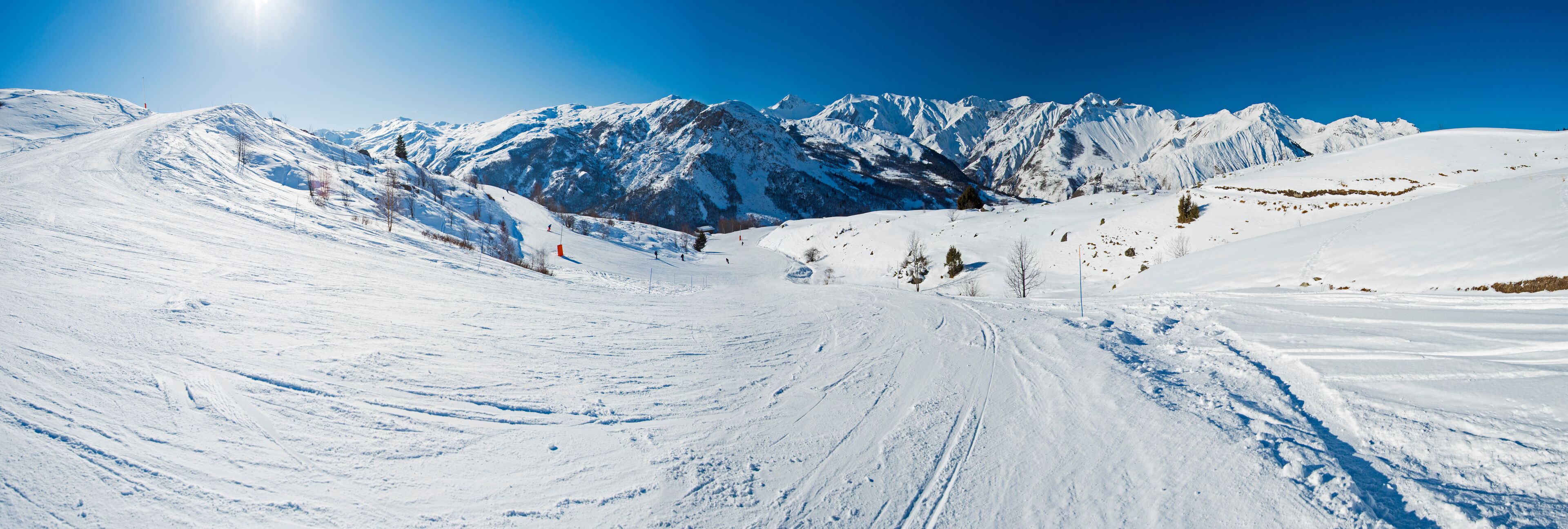 A snowy mountain landscape with ski tracks and a clear blue sky.