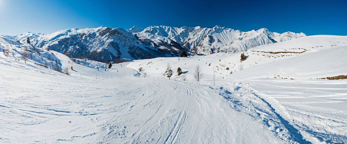 A snowy mountain landscape with ski tracks and a clear blue sky.
