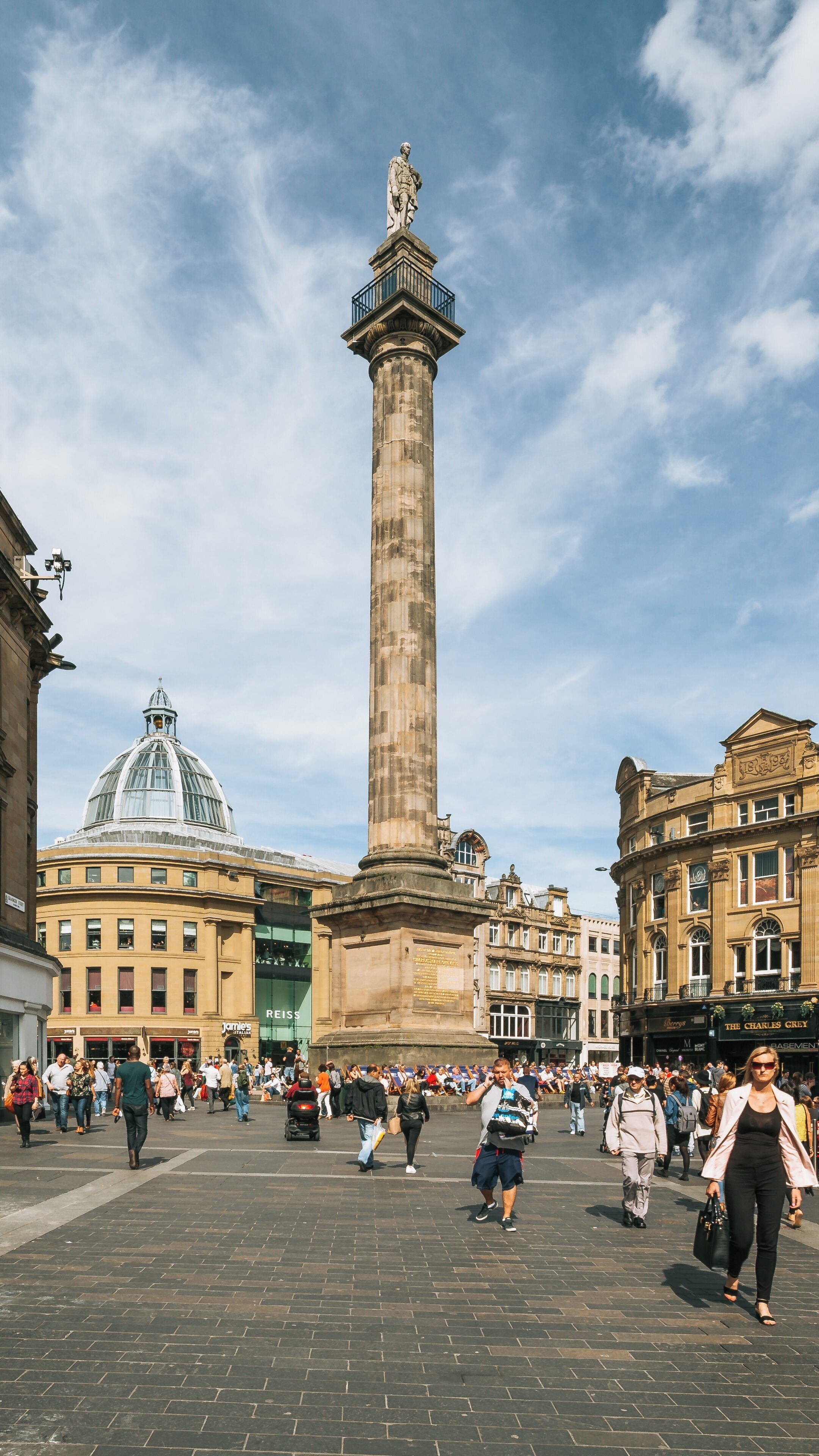 View of Grey's Monument surrounded by people in Newcastle City Center, Newcastle-upon-Tyne, England on a sunny day showcasing architectural beauty