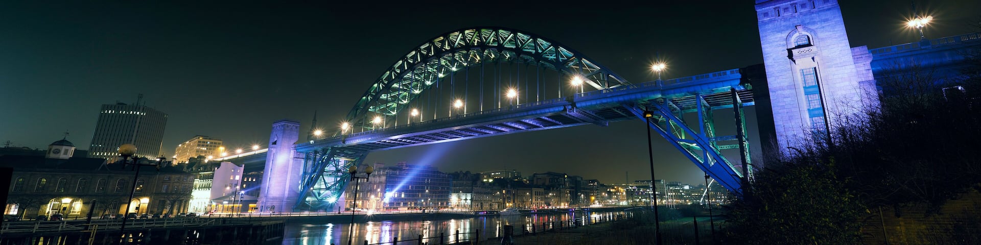 A brightly lit bridge with a distinctive arch and a clock tower.