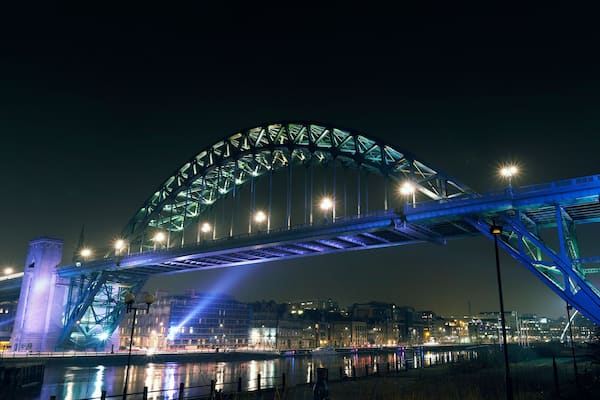 A brightly lit bridge with a distinctive arch and a clock tower.