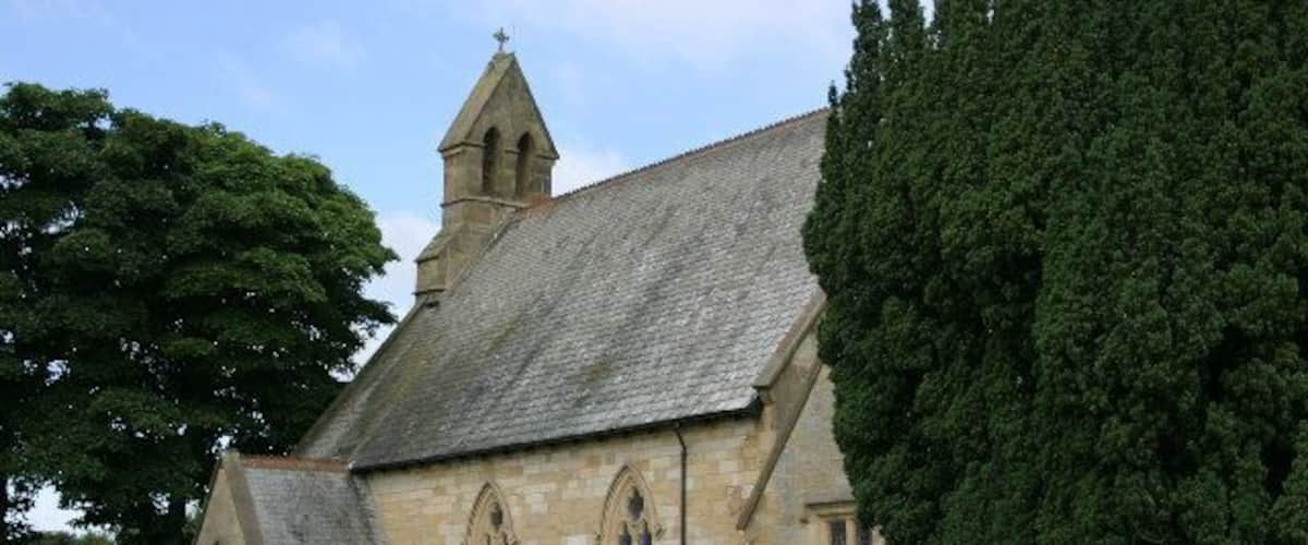 A church with a steeple, a graveyard, and a large tree.
