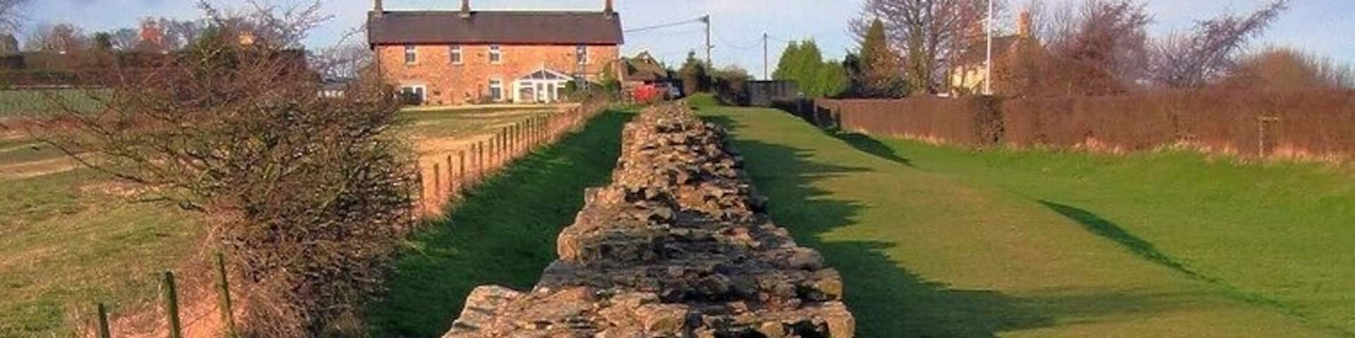 A stone wall leading to a house in a rural setting.