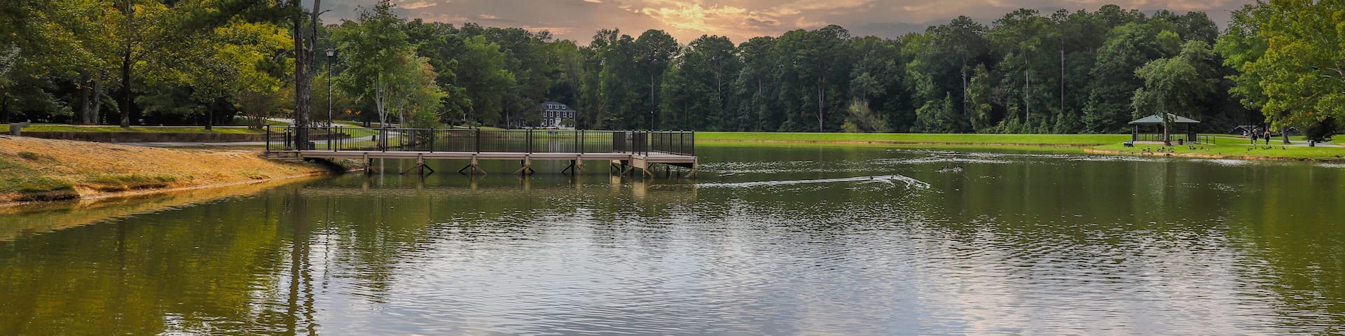 A serene lake with a wooden dock, surrounded by lush greenery and a cloudy sky.