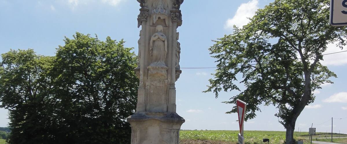 A stone monument with a cross at its top, surrounded by grass and trees.