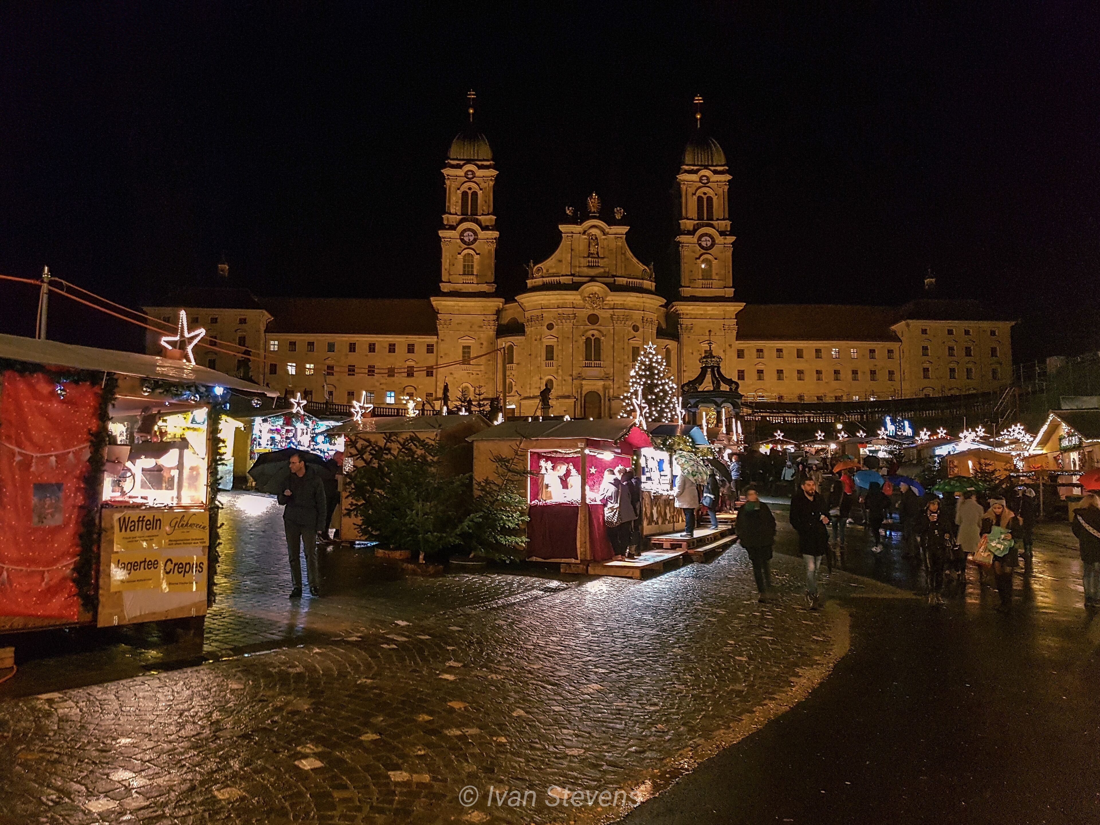 A nighttime market with stalls and a large building with two towers in the background.