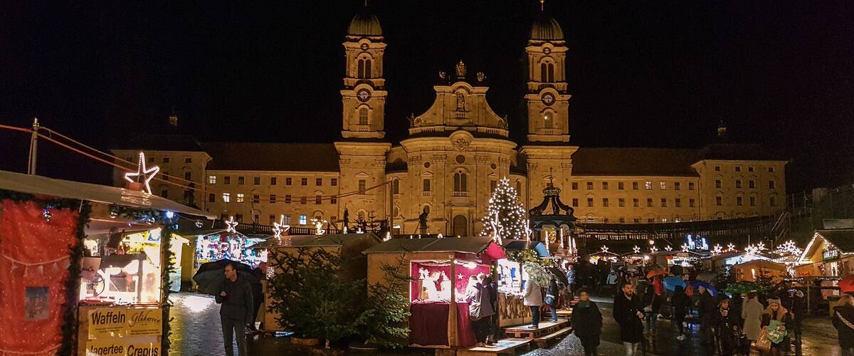 A nighttime market with stalls and a large building with two towers in the background.