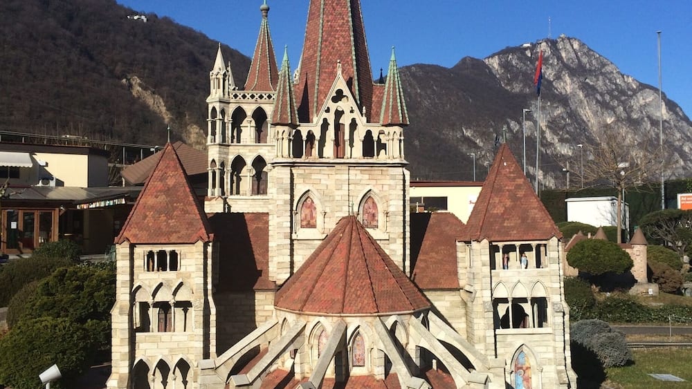 Une église historique, dotée d’un flèche imposante et de plusieurs tours, qui se dresse sur un arrière-plan montagneux.