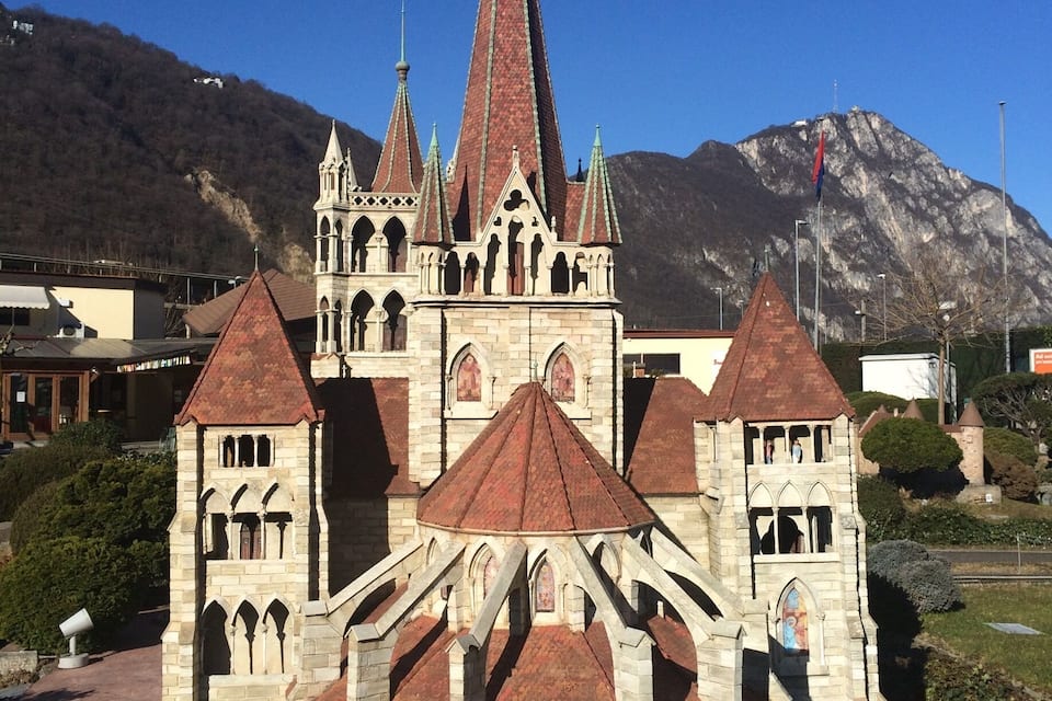 Eine historische Kirche mit einem hohen Turm und mehreren Belfurten, vor einer Bergkulisse gelegen.
