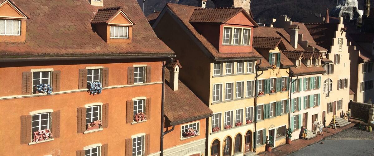 A row of colorful buildings with traditional architecture, a church tower, and a mountain in the background.