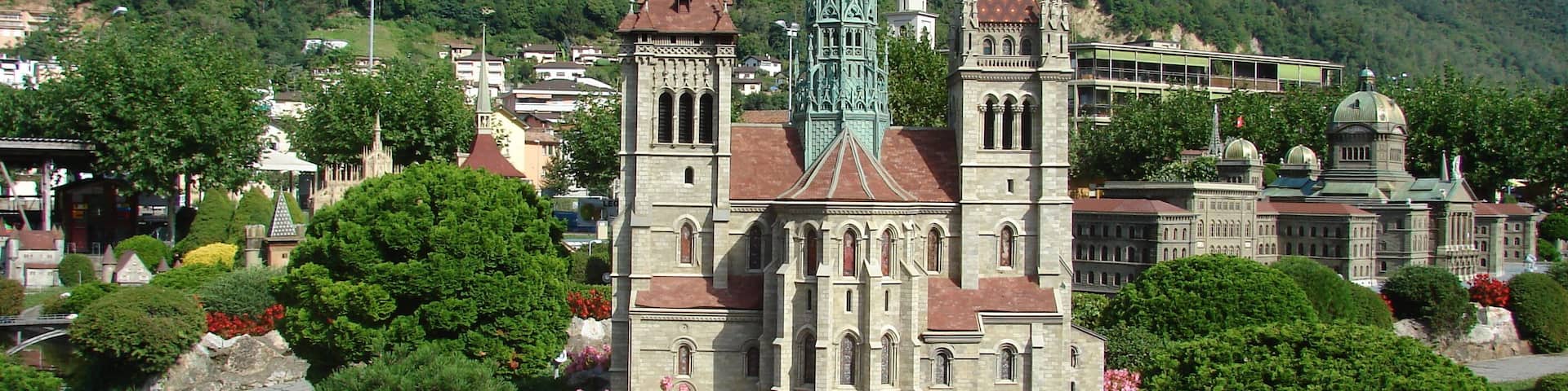 A historic church with a tall spire, surrounded by lush greenery and flowering plants.