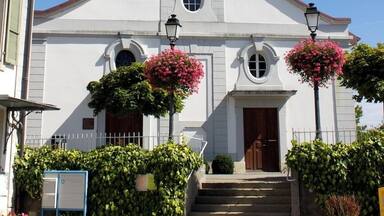 A white church with a clock tower, steps leading to the entrance, and pink flowers in planters.