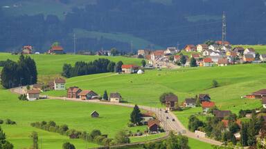 Un pueblo rural con campos verdes, casas y un camino sinuoso.