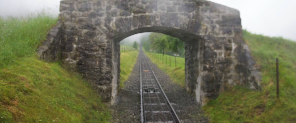 A stone railway bridge over tracks surrounded by grassy hills.