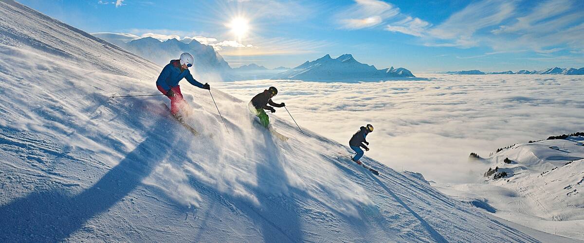 Skiers on a snowy mountain slope with a clear sky and distant mountains.