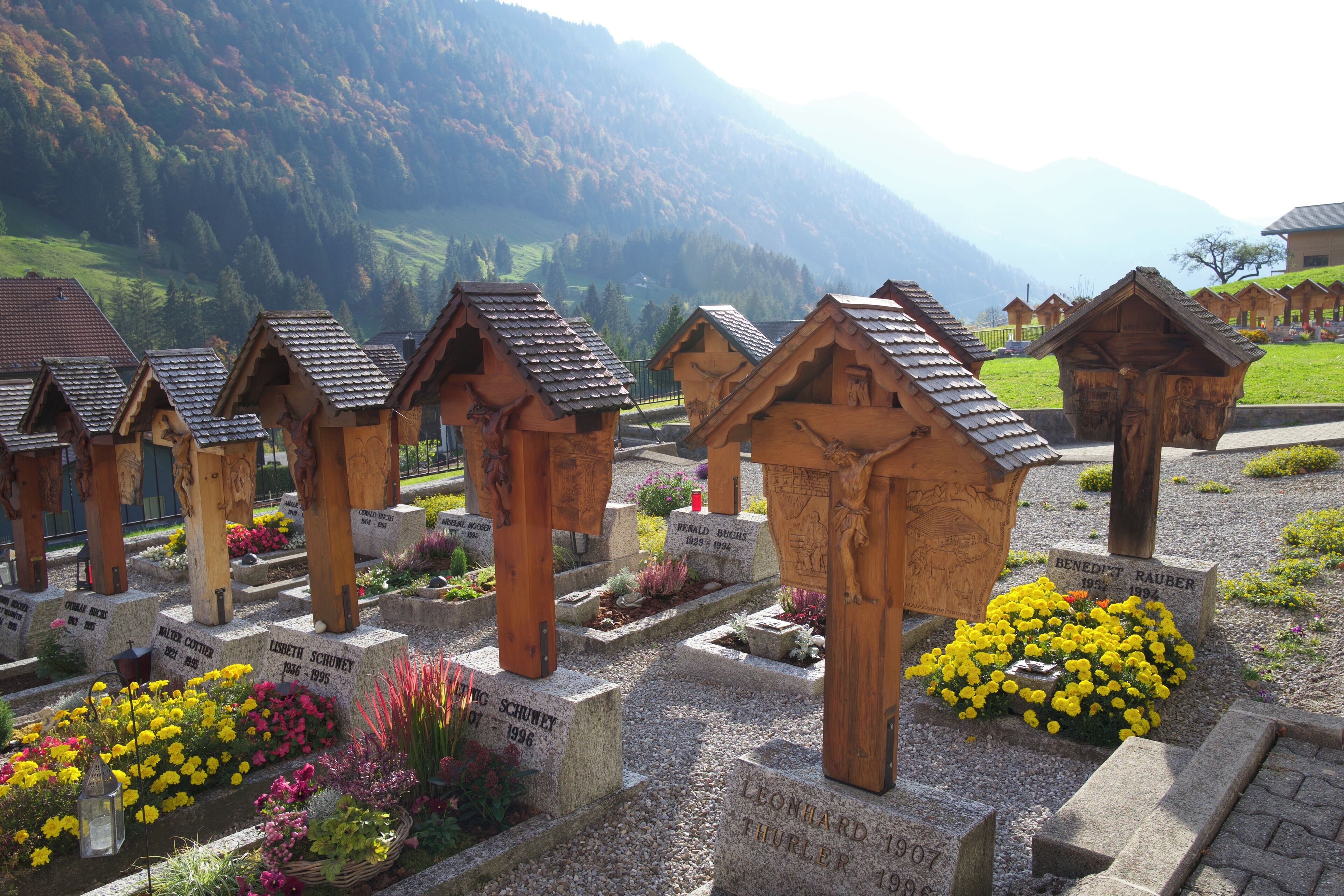 Wooden tombs with inscriptions, surrounded by colorful flowers and a mountainous backdrop.