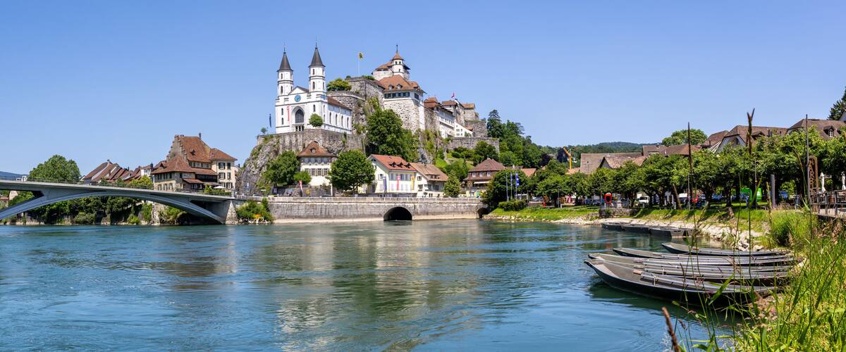 A river with a stone bridge, a castle, and boats.