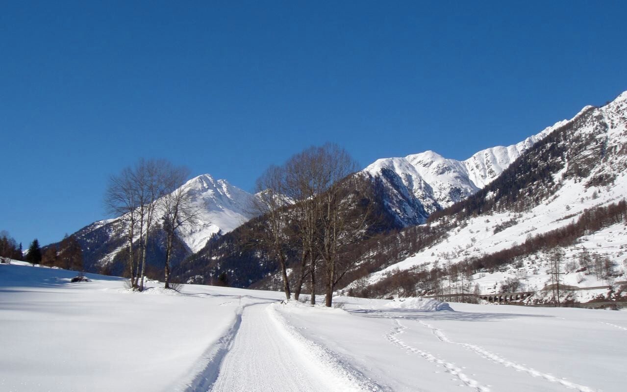A snow-covered road winding through a mountainous landscape with clear blue skies.