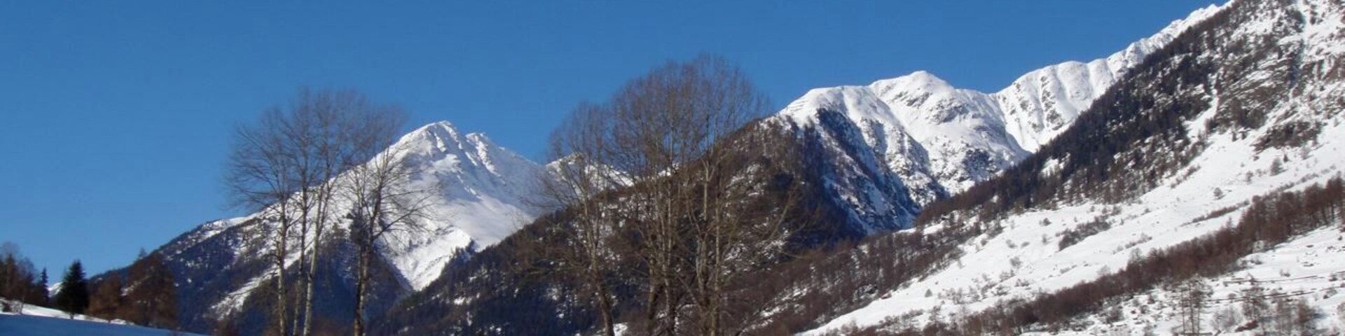 Una carretera cubierta de nieve serpentea a través de un paisaje montañoso bajo cielos azules despejados.