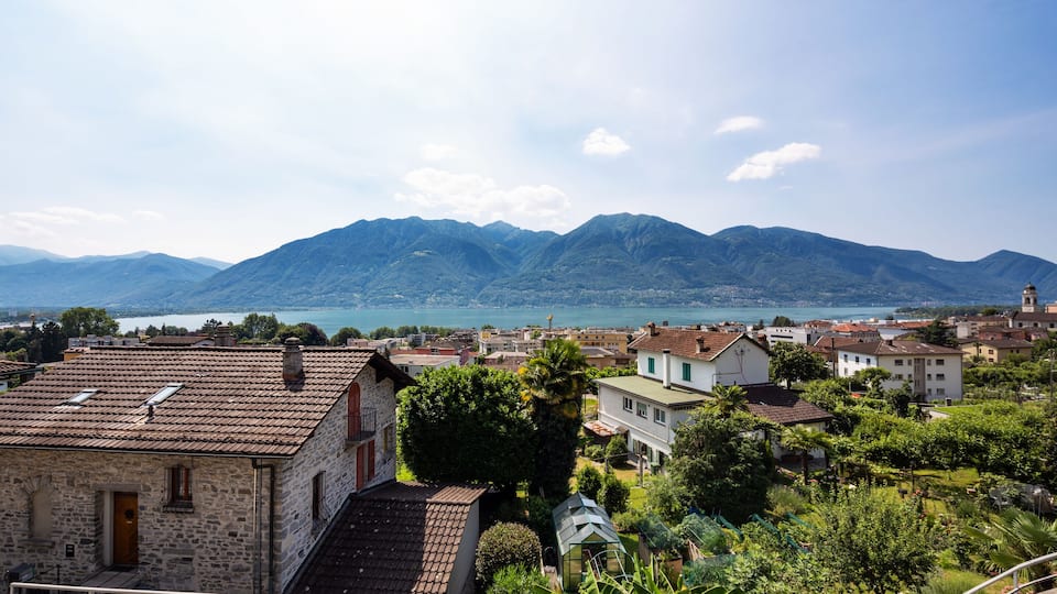 A town with stone buildings, a lake, and mountains in the background.