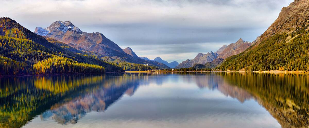 A calm lake surrounded by mountains with autumn foliage, reflecting the sky and landscape.