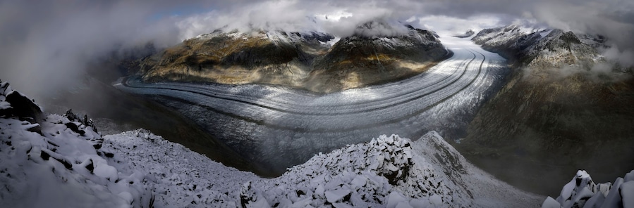 A glacier winding through a mountainous landscape with snow-covered peaks and valleys.