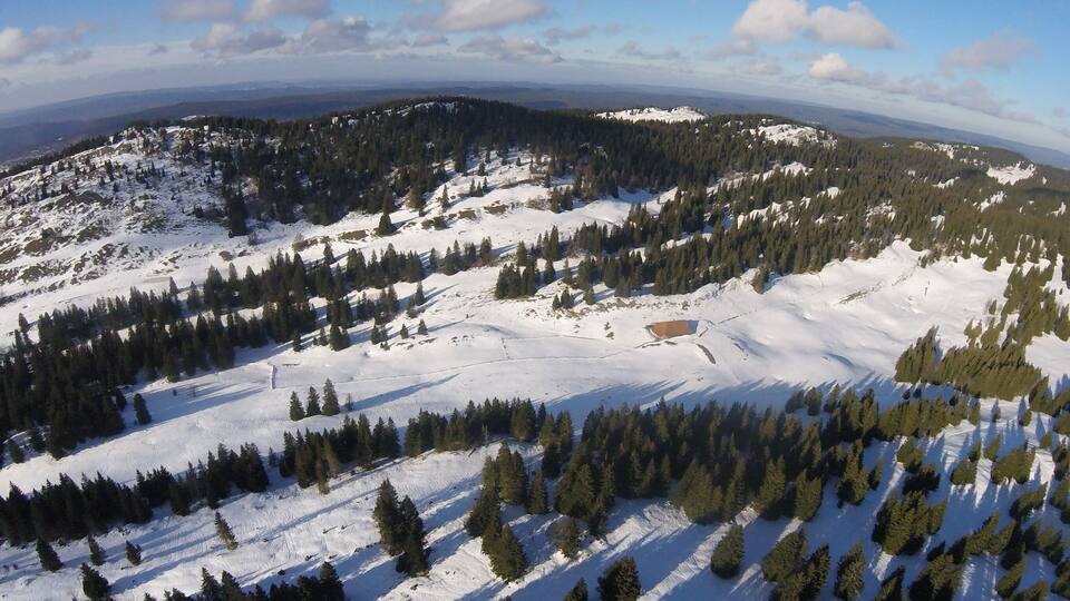 A snow-covered mountain landscape with dense forests and a clear sky.