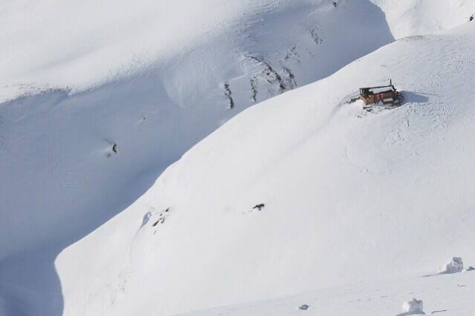 Een met sneeuw bedekte berg met een klein huisje en een piste.