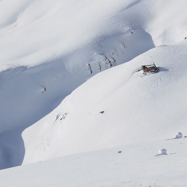 A snow-covered mountain with a small cabin and a ski slope.