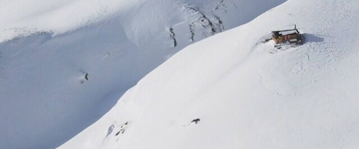 A snow-covered mountain with a small cabin and a ski slope.