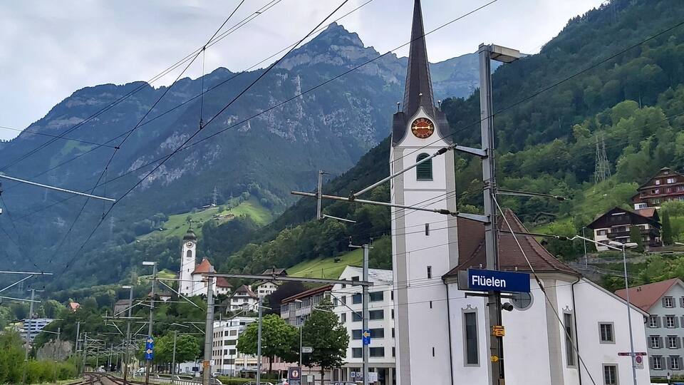 A railway station with tracks, a church, and mountains in the background.