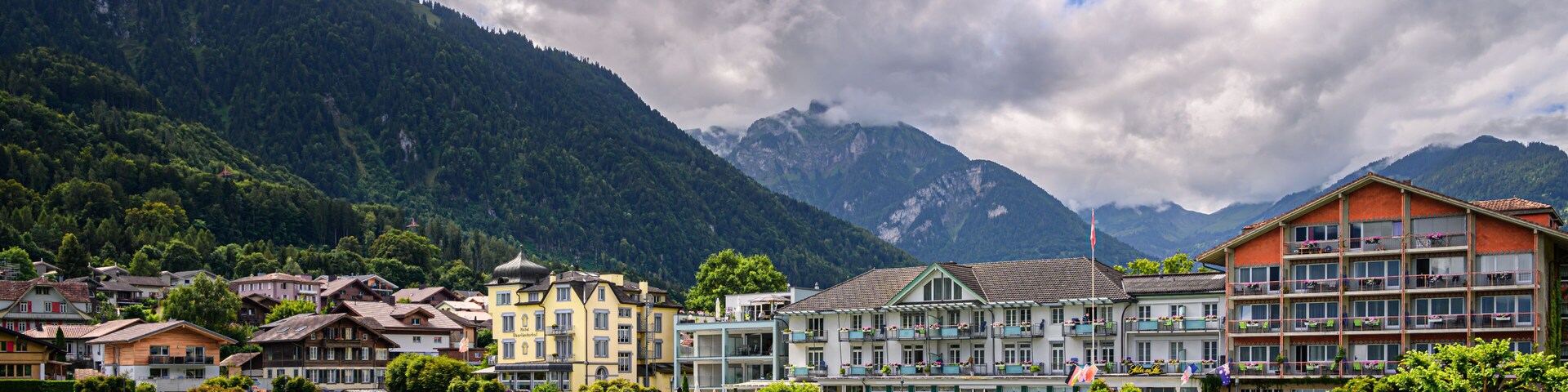 A lakeside town with colorful buildings, a river, and mountains in the background.