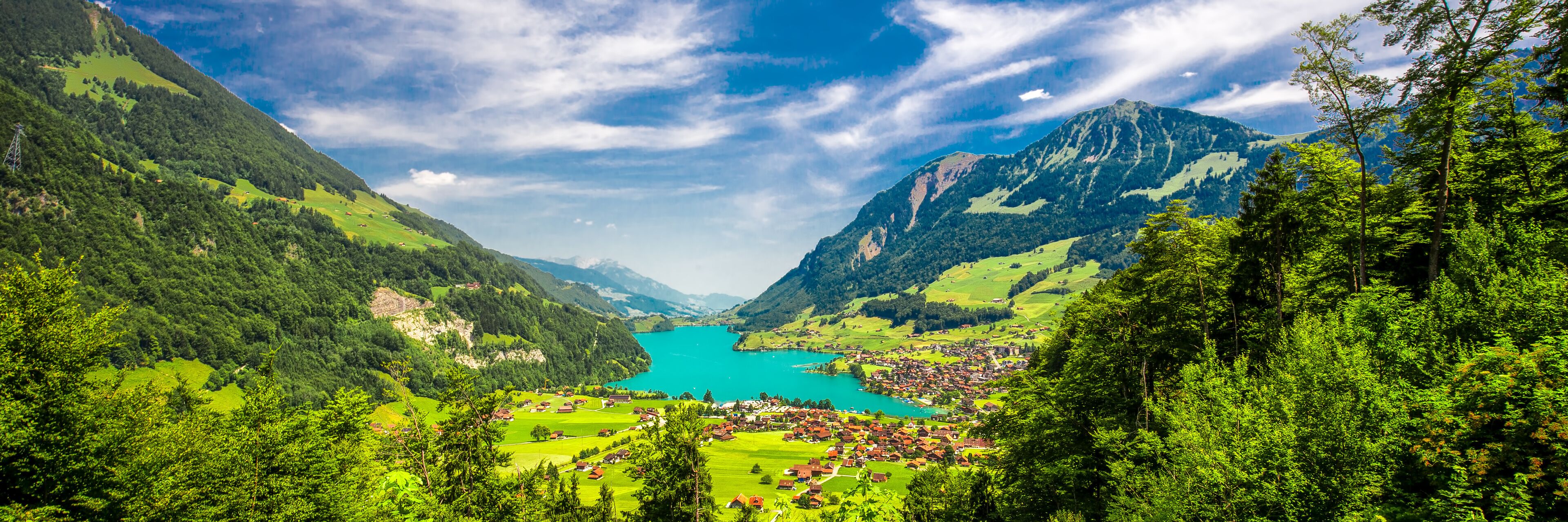 A mountainous landscape with a lake, green fields, and a small village.