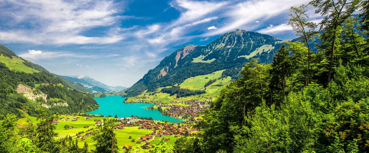 A mountainous landscape with a lake, green fields, and a small village.