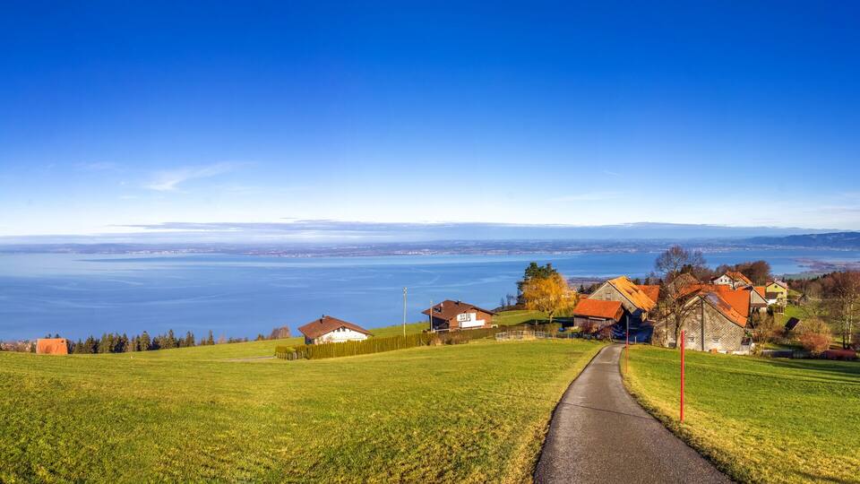 A scenic view of a green hillside with a pathway leading to a village by a lake.
